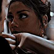 A GIF of Kathani Sharma in Bridgerton. She is making puppy dog eyes at Anthony Bridgerton who is offscreen. Their intertwined hands slowly lower from above their heads. End ID